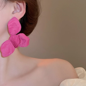 Close-up of a large magenta flower earring with painted petals worn by a fashion model