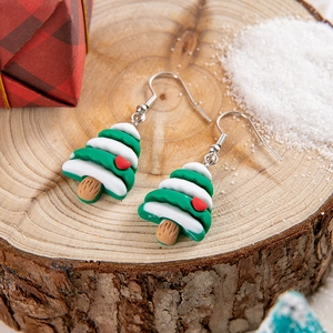 Macro shot of resin Christmas tree earrings on wood with festive snow and gift decor