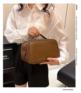 Detail of a brown PU leather toiletry bag featuring a wide handle and lucky tag