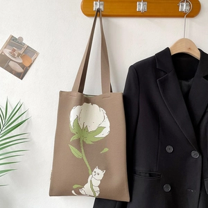 Detail view of khaki knit tote bag featuring white floral and cat motifs on a wooden hook