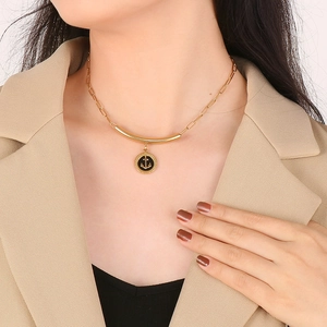 Detail of a gold anchor pendant with black enamel inlay on a paperclip chain necklace