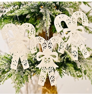 Glittery white candy cane ornaments with bows hanging on a snowy Christmas tree branch