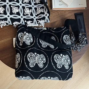 Close-up of black canvas bag with white butterfly embroidery on a rustic wooden table