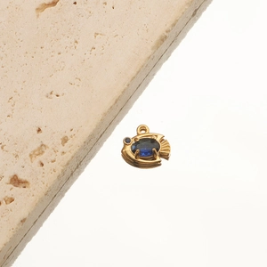 Detail of 18K gold plated fish pendant with sparkling blue gemstone on stone base