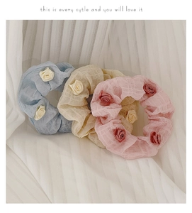 Detailed view of light blue, beige, and pink camellia flower scrunchies on soft white fabric