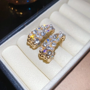 Close-up of gold C-shaped earrings with pearls and crystals in a white jewelry box