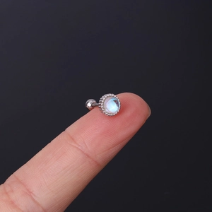 Close-up of small round moonstone stud earring with silver gear edge on a fingertip