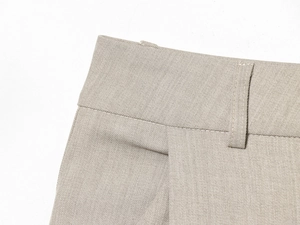 Close-up detail of beige pleated trousers showing waistband stitching and belt loops