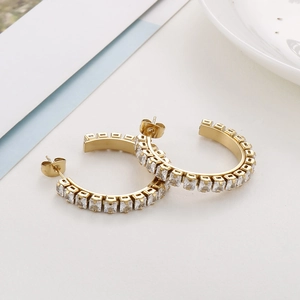 Macro detail of gold-plated C-shaped hoop earrings featuring square-cut white zircons
