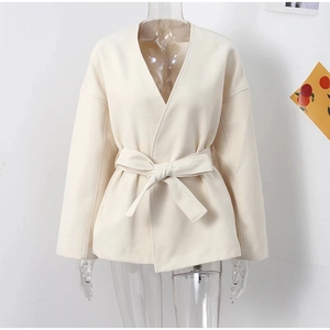 Detail view of cream white wool coat featuring a V-neckline and waist tie belt closure