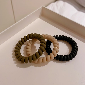 Three matte spiral phone cord hair ties in black, khaki, and dark green on a tray