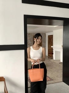 Detail shot of an orange hand-woven straw tote bag paired with a minimalist summer outfit