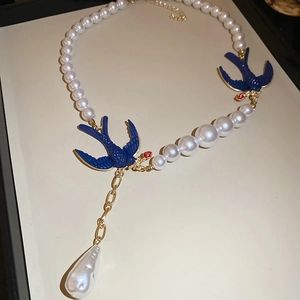 Detailed view of pearl necklace with blue swallow charms and a teardrop pearl pendant