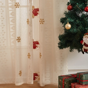 Close-up of beige Christmas lace curtain with reindeer and snowflake embroidery patterns