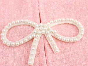 Detailed macro shot of pink tweed fabric texture with white pearl bow decoration