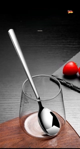 Polished stainless steel long handle spoon for stirring coffee in a glass cup