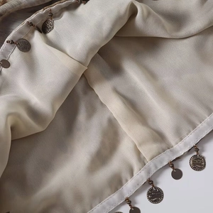 Detail of beige chiffon fabric with vintage metal coin charms and fine edge stitching