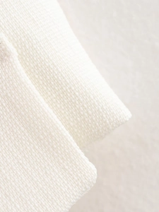 Macro shot of white knitted fabric texture showing thick edges and soft material weave