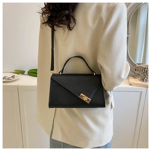 Detail of black crocodile texture bag with gold hardware worn over a cream blazer