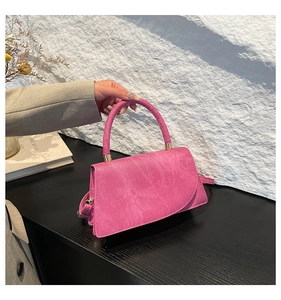 Close-up of rose pink suede handbag with curved handle and gold metal hardware