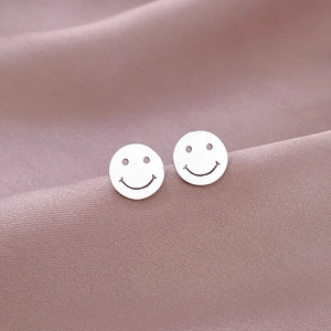 Macro view of silver round smiley face titanium steel stud earrings on pink satin
