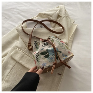 Detailed view of beige bucket bag with floral embroidery and brown leather strap on blazer