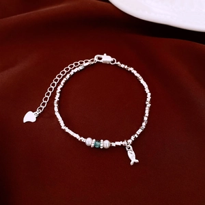 Dettaglio del bracciale d'argento con ciondolo a pesce e cuore su tessuto rosso