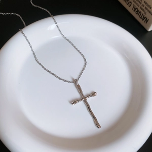 Detailed view of silver liquid metal cross pendant on a white ceramic plate