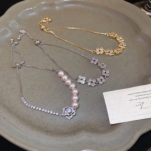 Detailed shot of French style floral zircon bracelets and pink pearl charms on a ceramic tray