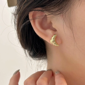 Macro detail of gold croissant hoop earrings with textured metallic finish on model