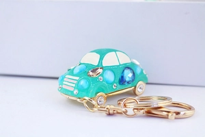 Close-up of a teal car keychain with colorful gemstones and rhinestones on gold hardware