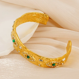 Detail of vintage gold textured bangle with evil eye design and green gemstone