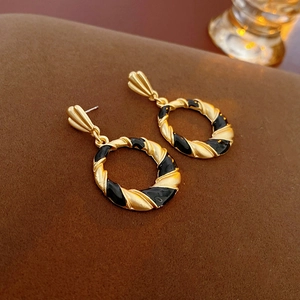 Detail of vintage twisted gold metal earrings with black enamel on a textured background