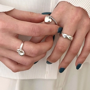 Close-up of S925 silver rings with quilted pattern, heart charm, and twisted knot design