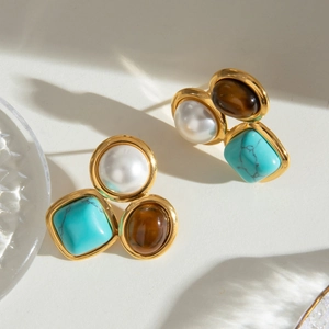 Détail de boucles d'oreilles rétro avec turquoise, perle et œil de tigre sur monture dorée
