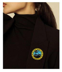 Detail view of a yellow enamel cat society brooch pinned on a dark suit lapel