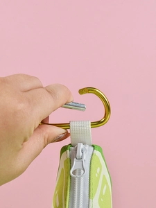 Detail of lime patterned pet waste bag dispenser showing metal carabiner hook and zipper