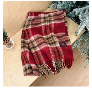 Detail of red plaid winter scarf with fringe and leather label on wooden background