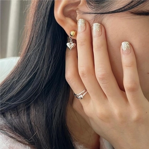 Detail of twisted knot silver ring and gold ball stud earring set on female model