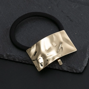 Eleganter goldener Metallhaargummi mit strukturierter Oberfläche auf schwarzem Haarschmuck