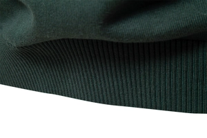 Gros plan du poignet côtelé vert foncé et du tissu en maille texturé de ce pull-over