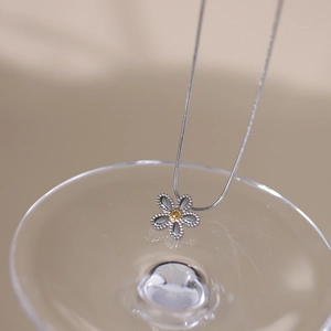 Close-up of a silver daisy necklace with a gold core hanging on a glass rim
