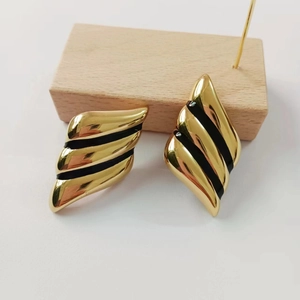 Detailed close-up of 18K gold plated wing earrings with black enamel on a wooden display