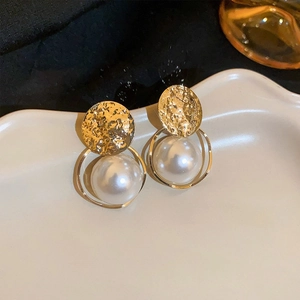 Detail of gold hammered metal earrings with elegant pearl drop on a ceramic tray