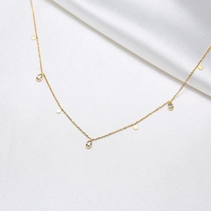Close-up of gold titanium steel necklace with zircon drops and round sequins on white fabric
