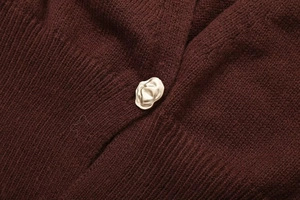 Close-up of golden lava-textured button on burgundy knitwear with detailed texture