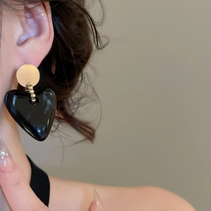 Close-up of a glossy black heart earring with gold accents worn by a model