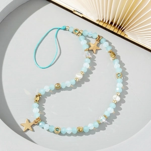 Light blue beaded phone strap with gold star pendant and white pearls on a tray