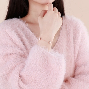 Rose gold chain bracelet featuring cartoon figure charms worn over a pink sweater