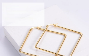 Macro shot of large polished gold square hoop earrings on a textured stone display